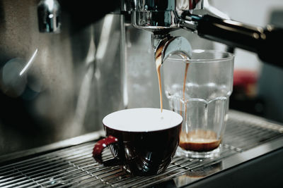 Close-up of coffee pouring in cup and drinking glass