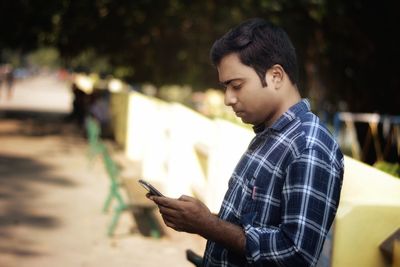 Side view of young man using mobile phone outdoors