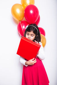 Portrait of a beautiful young woman sitting on book against white background