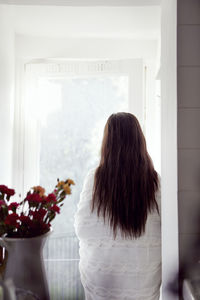 Woman wrapped in blanket standing looking through window