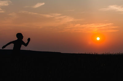 Silhouette boy running on field against orange sky during sunset