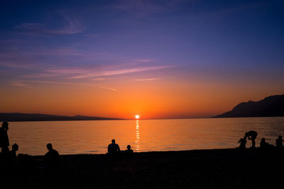 Silhouette of people on beach against sky during sunset