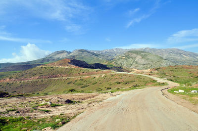 Dirt road by mountains against sky