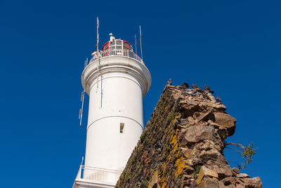 Low angle view of lighthouse by building against clear blue sky