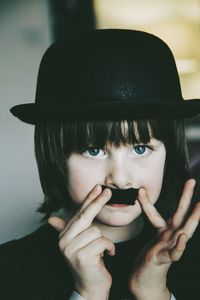 Close-up of cute boy holding mustache at home