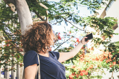 Mature woman taking selfie by tree in city