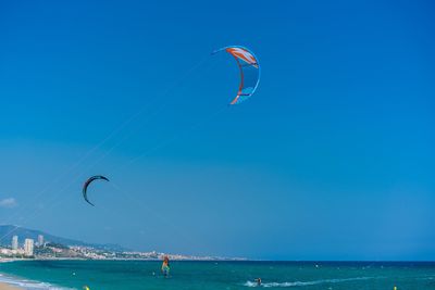 People paragliding at beach against blue sky