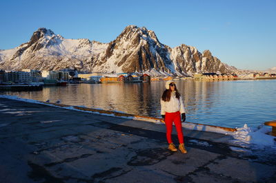 Full length of woman standing against snowcapped mountain by lake