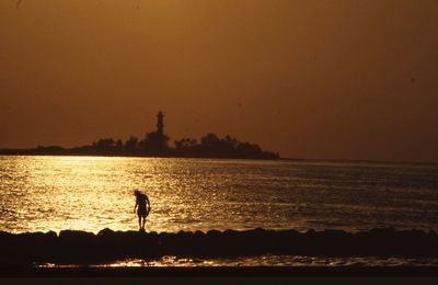 Silhouette man standing by sea against orange sky