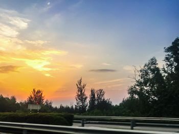 Road by trees against sky during sunset