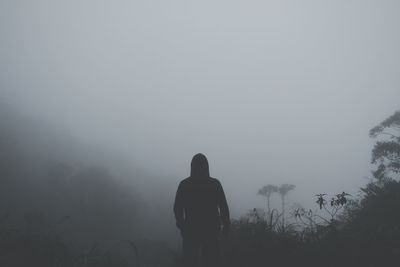 Rear view of silhouette man standing on landscape in foggy weather