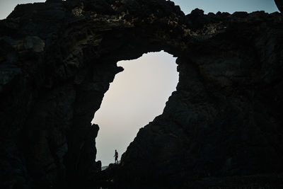 Side view of anonymous male tourist near high rough rocky formation with hole in fuerteventura in canary islands spain