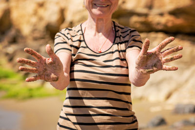 Elderly unrecognizable woman showing her palm hands covered in sand