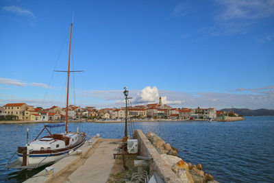 Sailboats moored at harbor by sea against blue sky