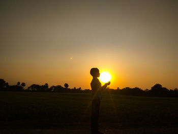 Silhouette man standing on field against sky during sunset