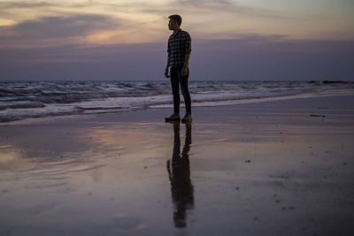 Rear view of man standing on beach during sunset