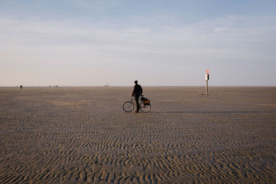 Man riding bicycle on sand against sky