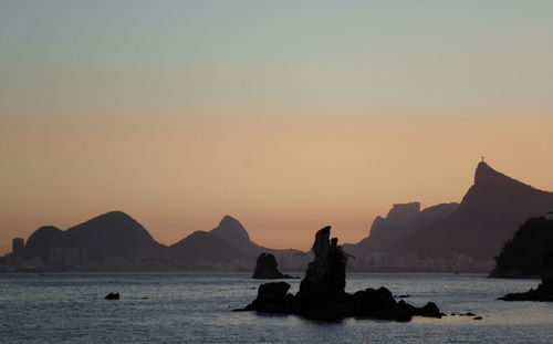Silhouette rocks in sea against sky during sunset