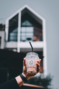 Close-up of hand holding drink against built structure