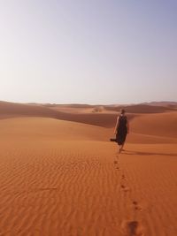 Rear view of man on sand dune in desert against clear sky