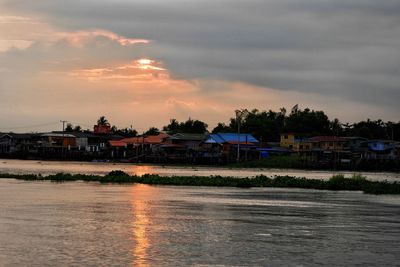 Scenic view of river by buildings against sky during sunset