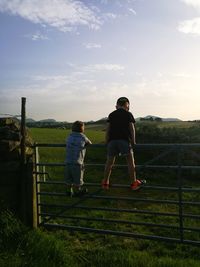 Rear view of siblings standing on railing against sky