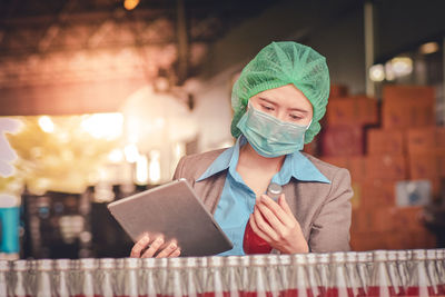 Woman using digital tablet while inspecting drinks in factory