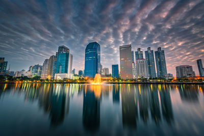 Reflection of illuminated buildings in city against sky during sunset