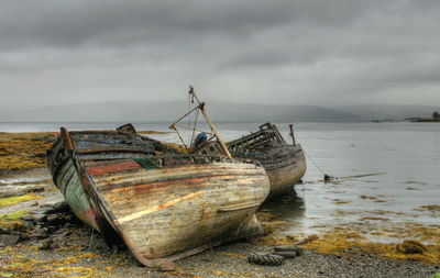 Abandoned boat on shore by sea against sky