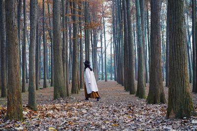 Side view of woman walking amidst trees in forest