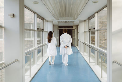 Full length rear view of male and female doctors discussing while walking together in hospital corridor