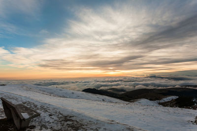 Snow covered landscape against sky during sunset