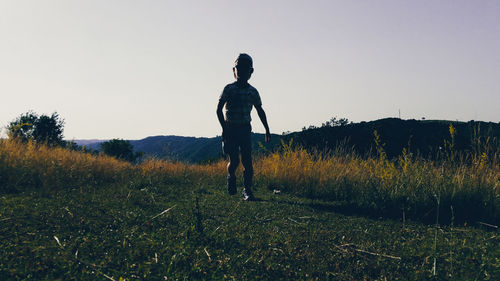 Silhouette boy walking on grassy field against clear sky