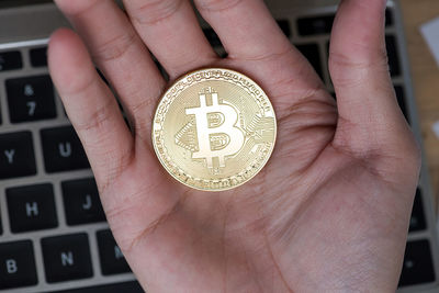Cropped hand holding bitcoin over laptop