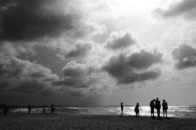 People standing at beach against cloudy sky