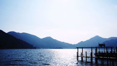 Pier by river against mountains and sky on sunny day