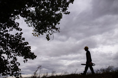 Low angle view of silhouette man standing by tree against sky