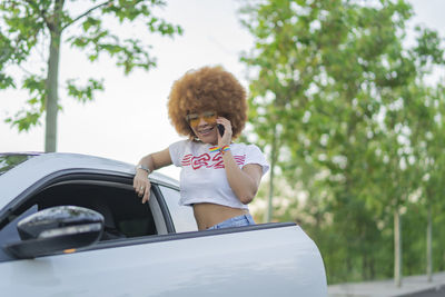 Woman with afro hair talking on the phone next to her car