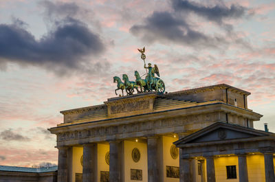 Low angle view of illuminated brandenburg gate against cloudy sky during twilight, berlin, germany