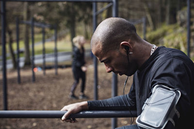 Side view of male athlete wearing headphones while exercising on parallel bars in forest