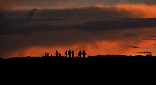 Silhouette people on landscape against orange sky