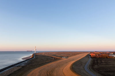 Road by sea against clear sky during sunset