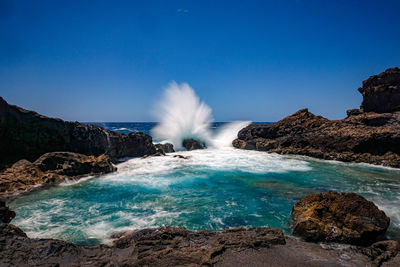 Scenic view of rocks in sea against clear blue sky