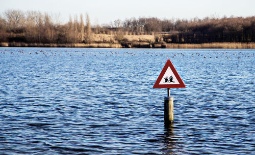 Warning sign by lake against sky