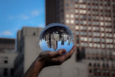 Close-up of hand holding glass against building in city