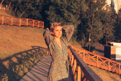 Portrait of beautiful young woman standing by railing against trees