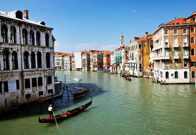 Gondolas moving on grand canal amidst buildings against clear blue sky