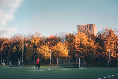 Man playing soccer on field by trees in city sky