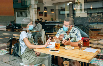 Friends wearing masks sitting in cafe seen through window