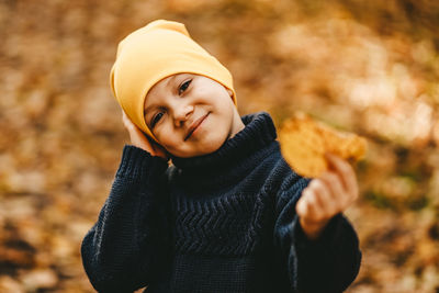 Portrait of a boy child in a warm hat walking holding an autumn leaf in the fall forest outdoors
